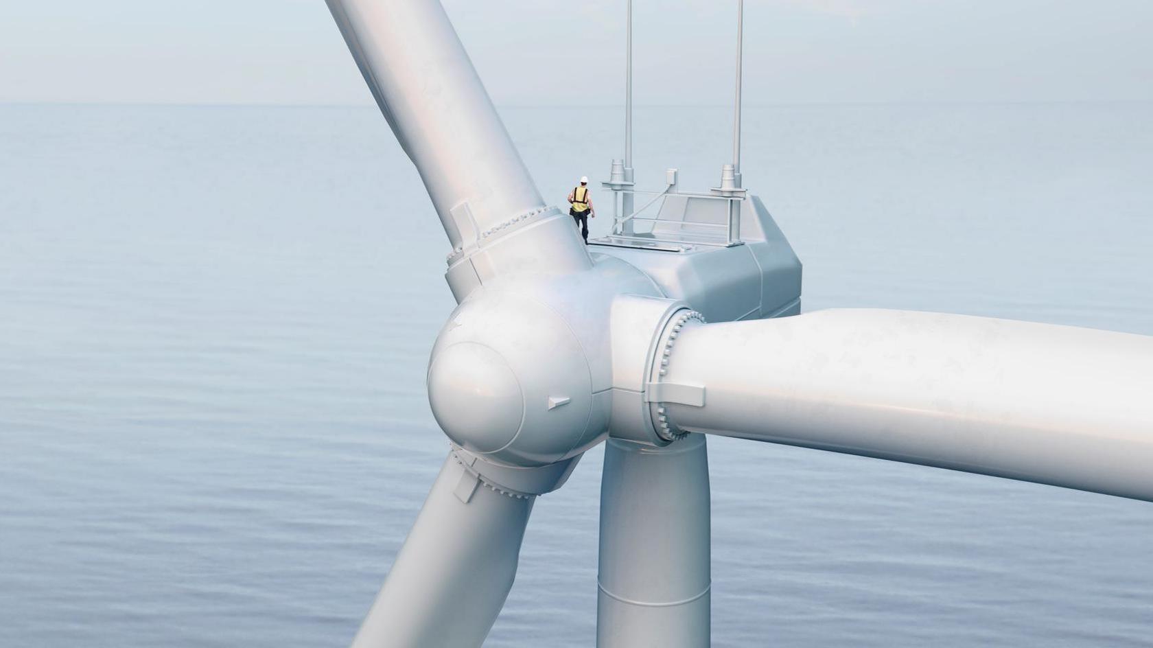 A technician, wearing a hard hat and safety clothing, on top of an offshore wind turbine. The sea stretches to the horizon.