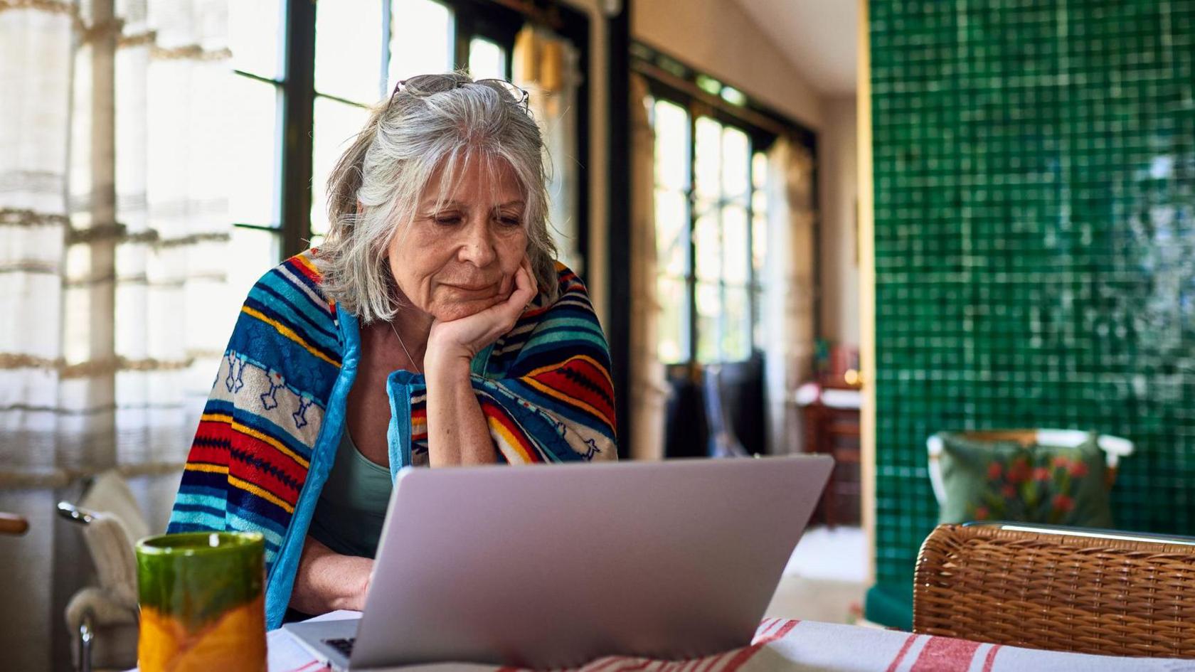 An older woman sitting at a table looking at a laptop