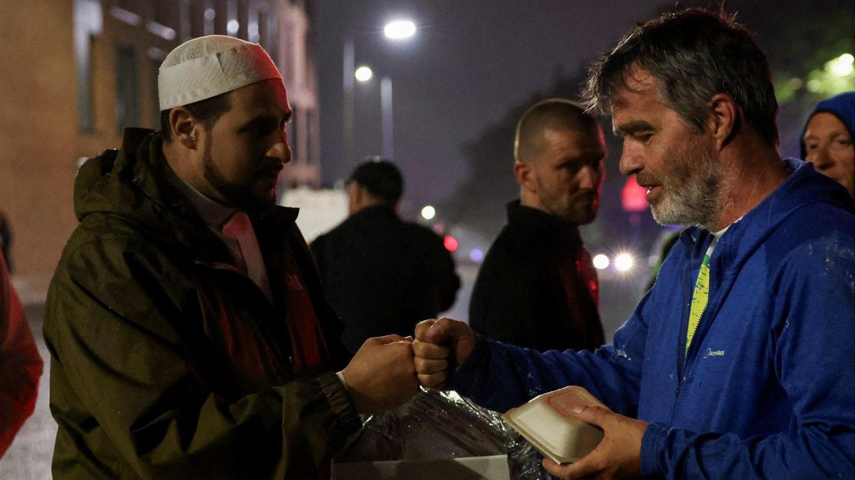 Imam Adam Kelwick fistbumps a protester as he hands out food during a protest