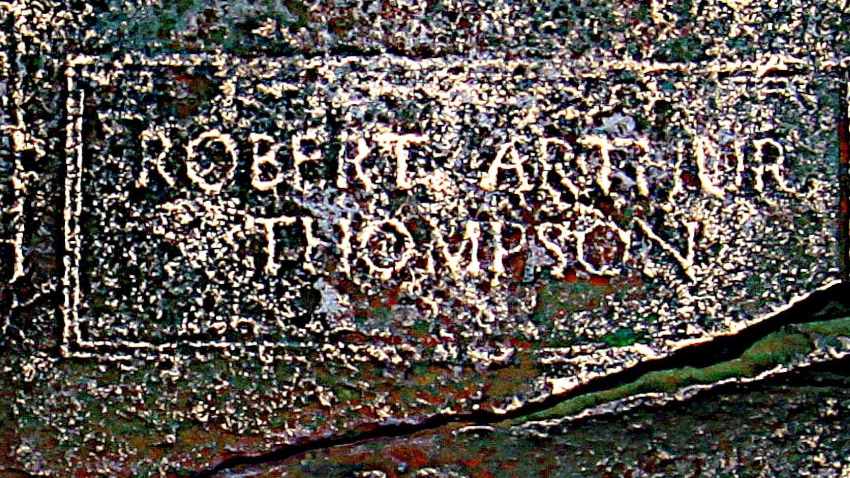 Part of a bronze plaque showing signs of wear and the name Robert Arthur Thompson