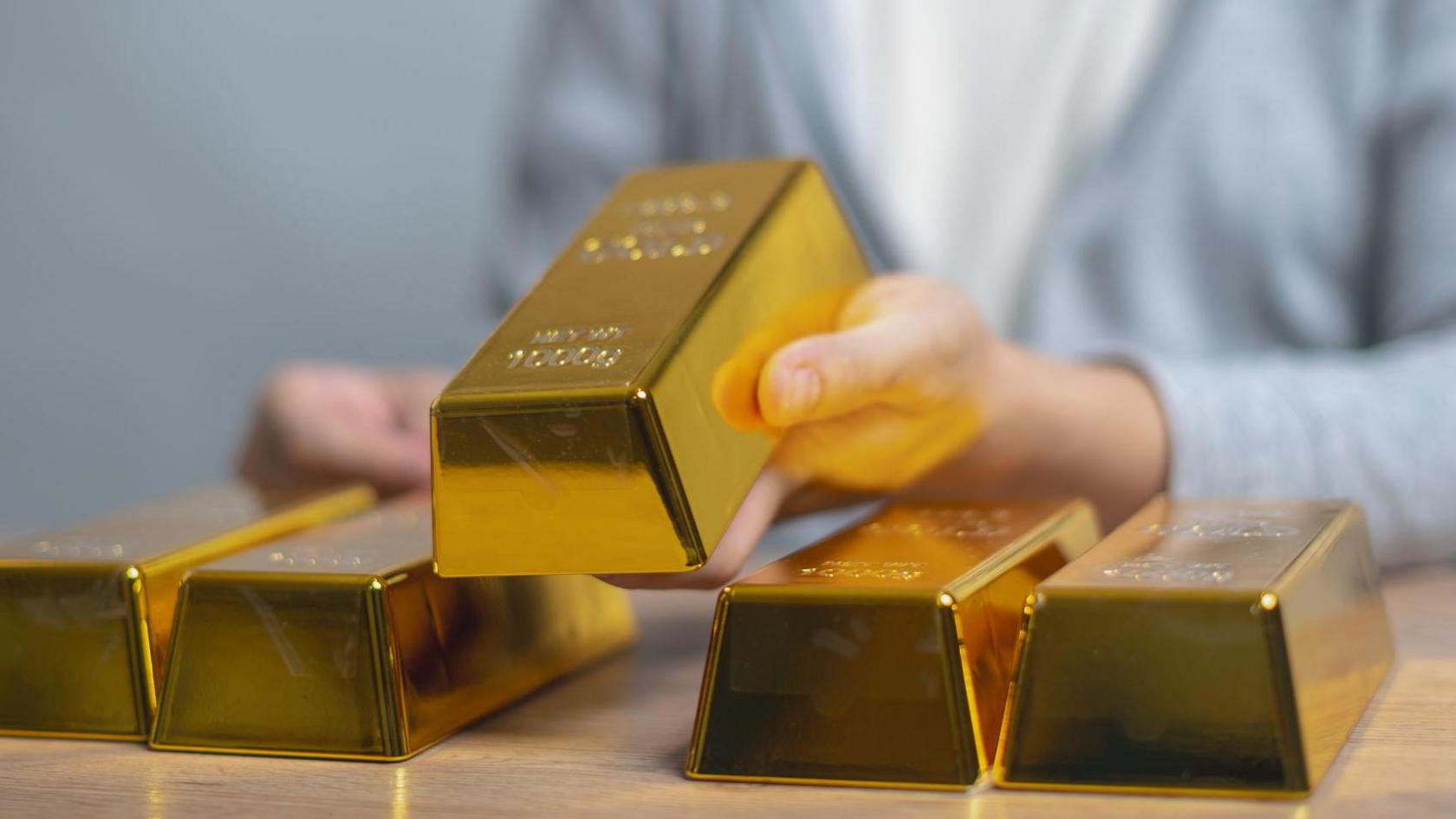 A person holds up a gold bar off table 