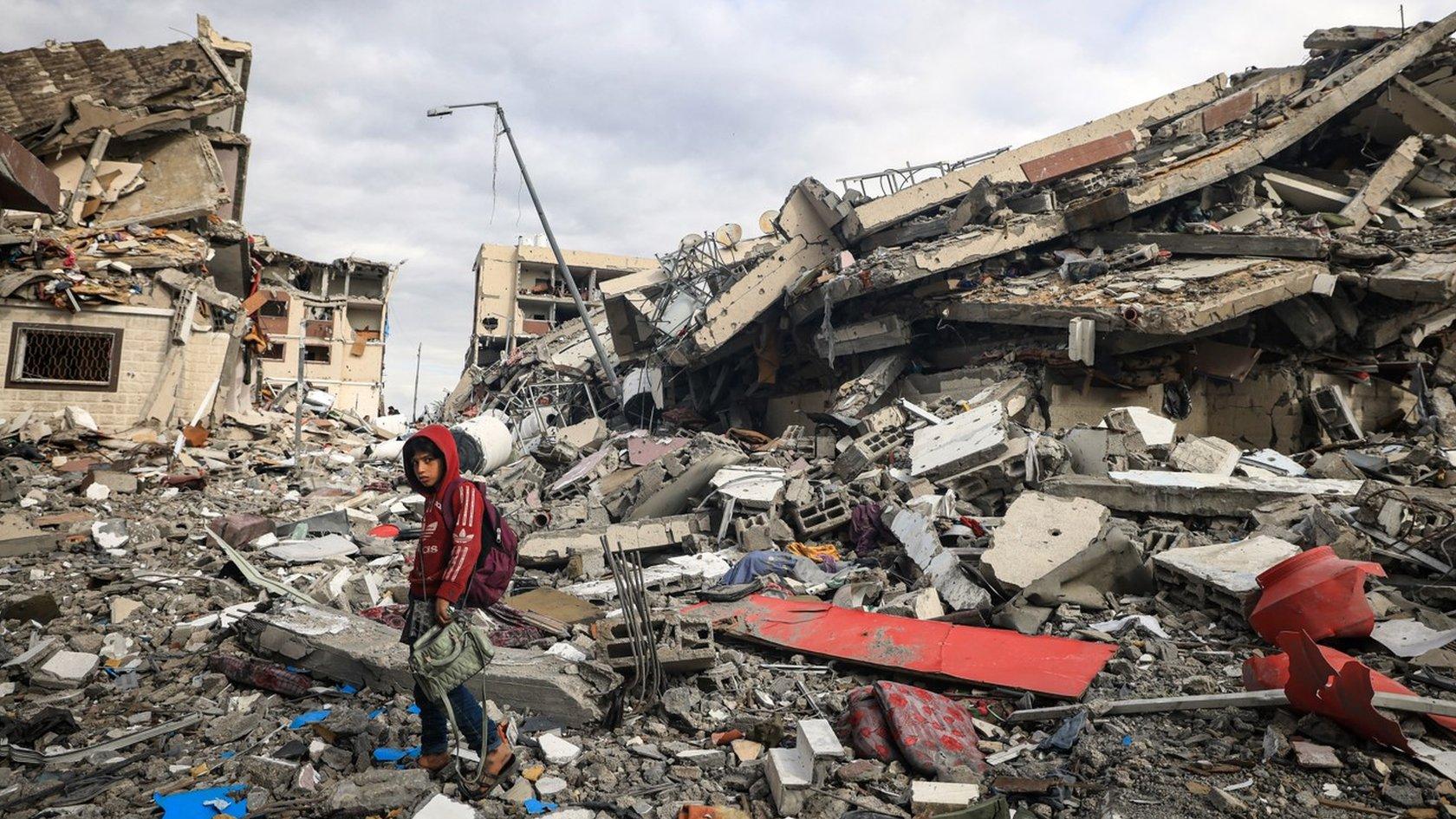 A Palestinian boy walks past destroyed buildings in the central Gaza Strip (28 November 2023)