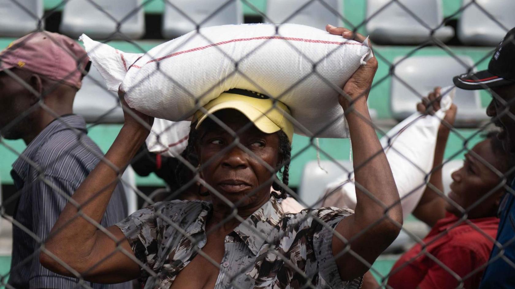 A woman receives food during a solidarity day organized by the Haitian government in Port-au-Prince, Haiti on 31 December 2024.  She carries a sack on her head.