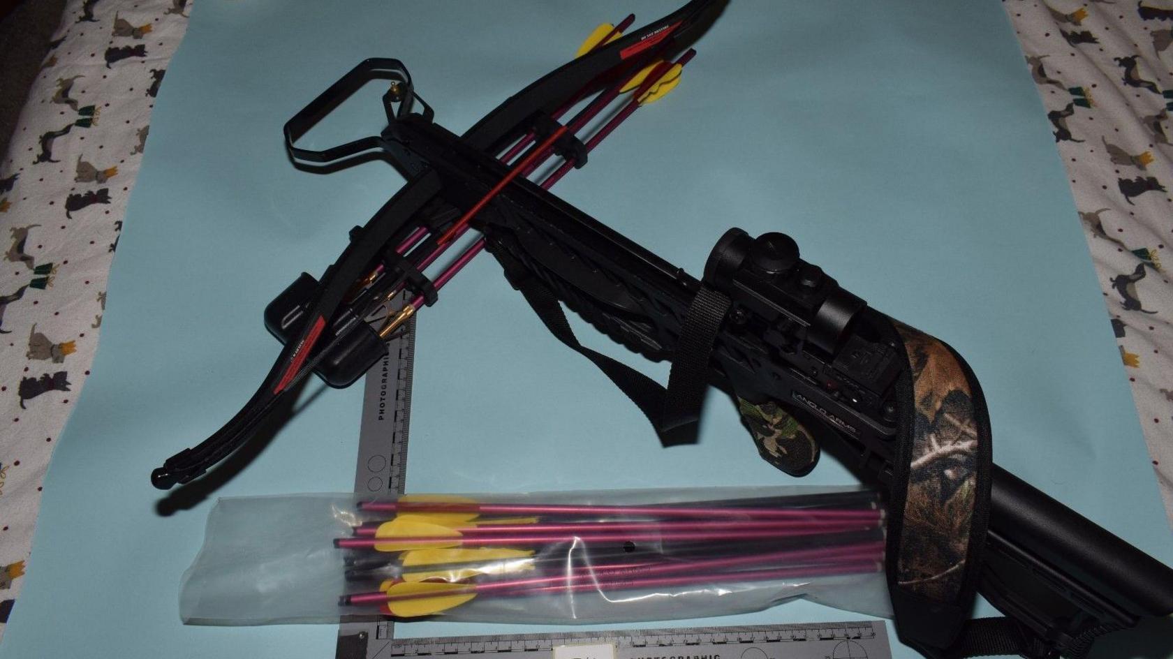 A crossbow with arrows in a packet, lying on a light-coloured sheet.