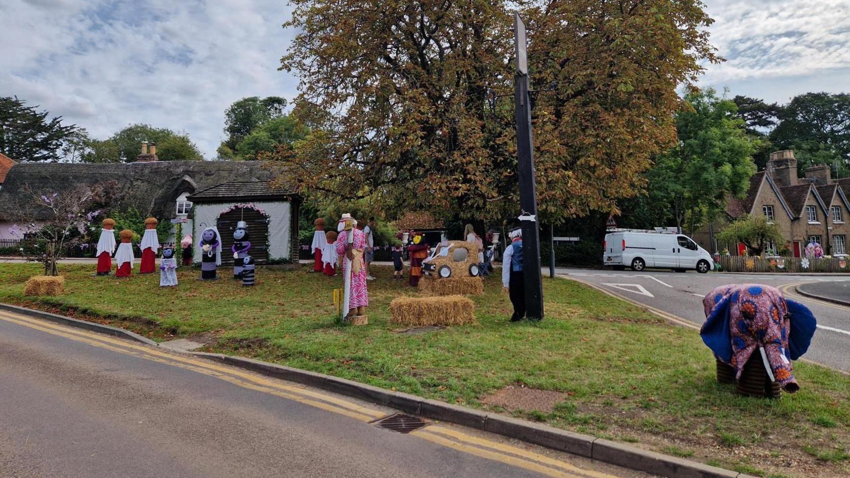 A village green, showing various scarecrows including people in a church, some bees dressed in wedding attire and an elephant.