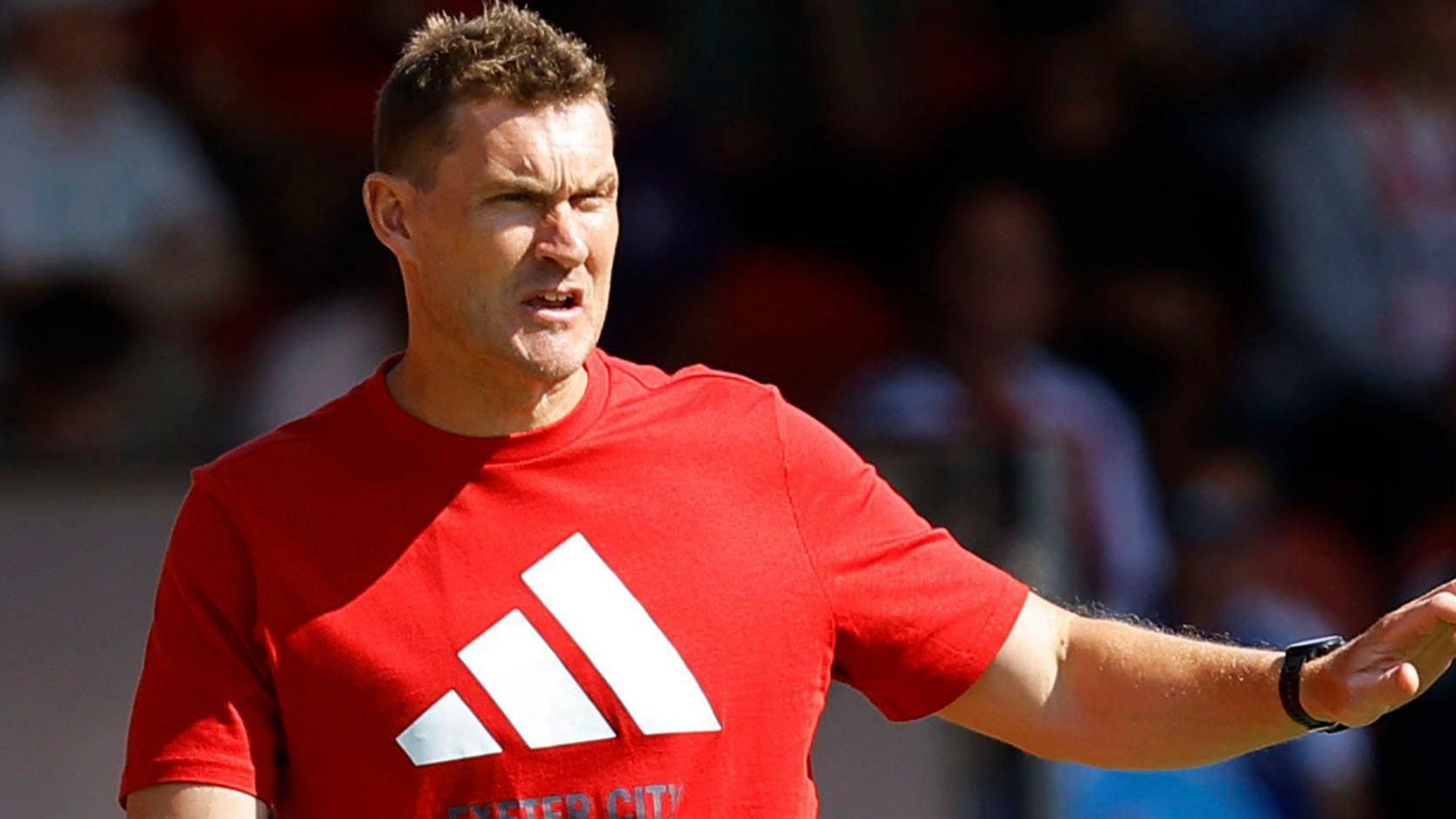 Matt Taylor points out some instructions to his players. He is wearing a red t-shirt.