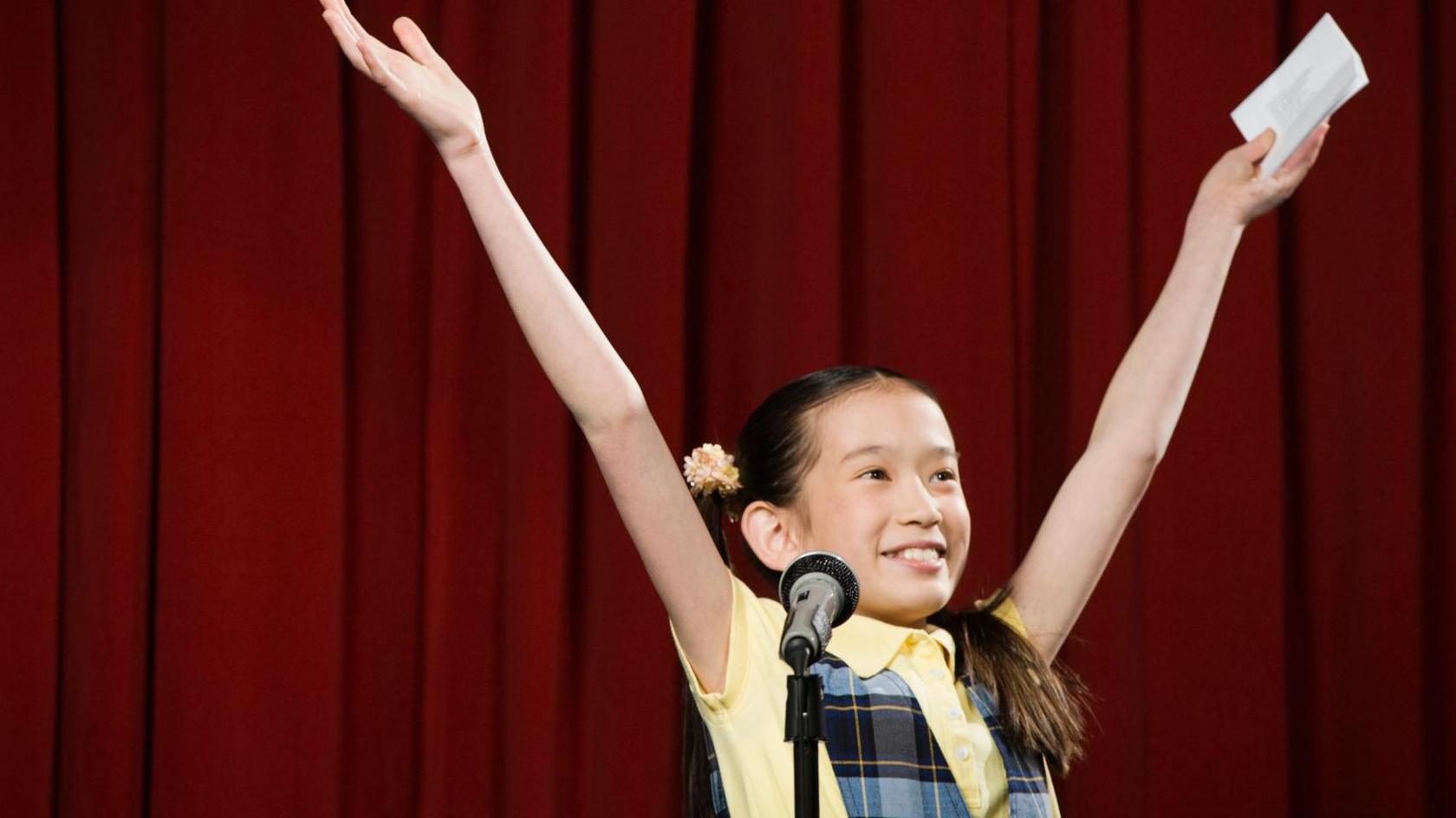 A child celebrates after performing on the stage, with a microphone in front of them.