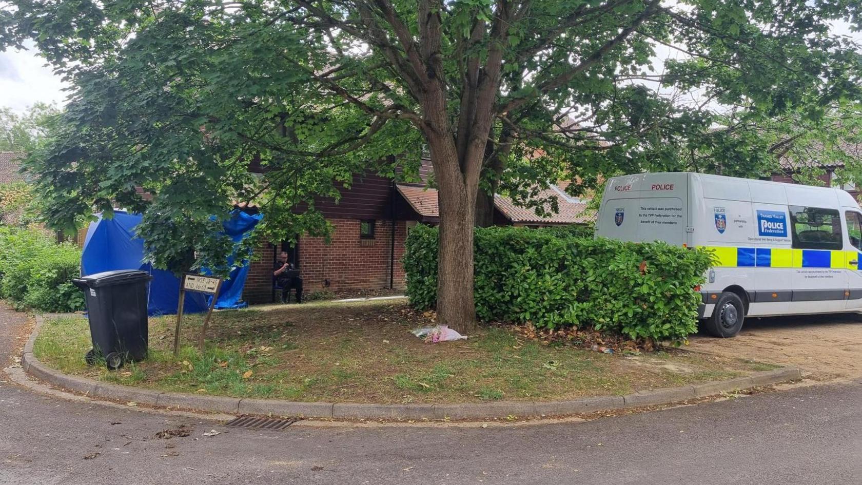A police van and blue tent outside a house, with a police officer sat outside a door.