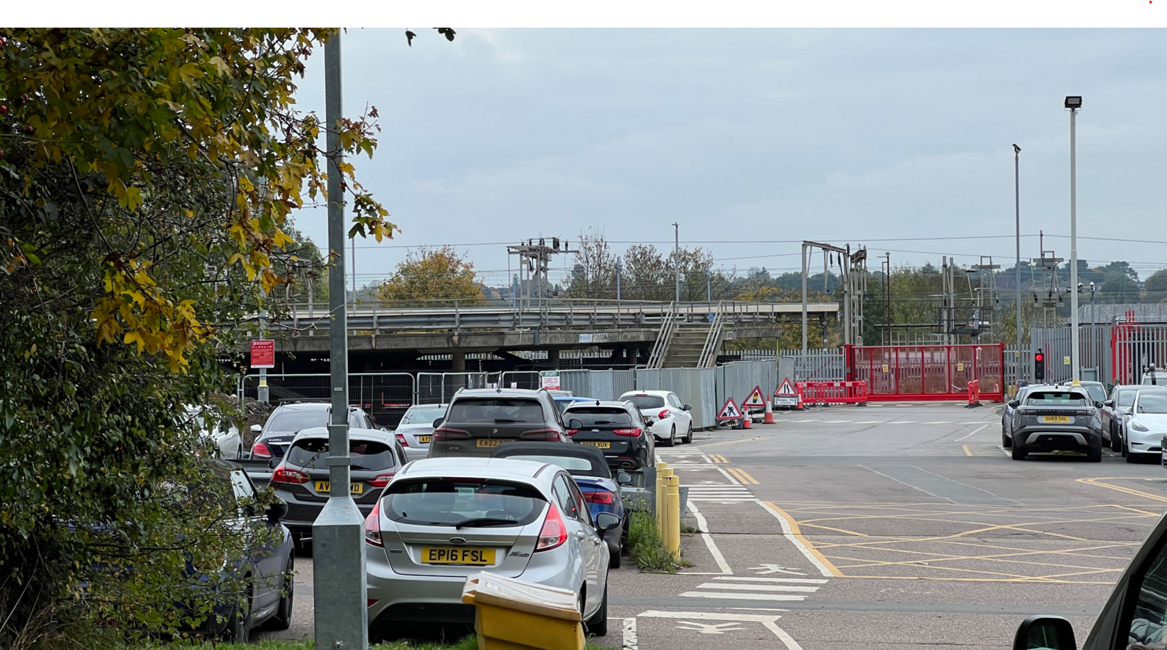 Ground level car park in foreground with empty concrete first floor in distance close to railway lines. 