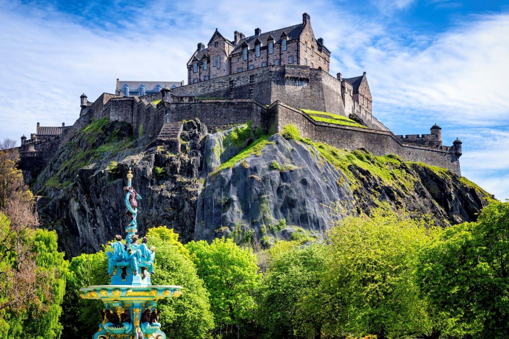 A view of Edinburgh Castle on a sunny day. The Ross Fountain is in the foreground and the netting over the rockface of the castle is visible in the background. 