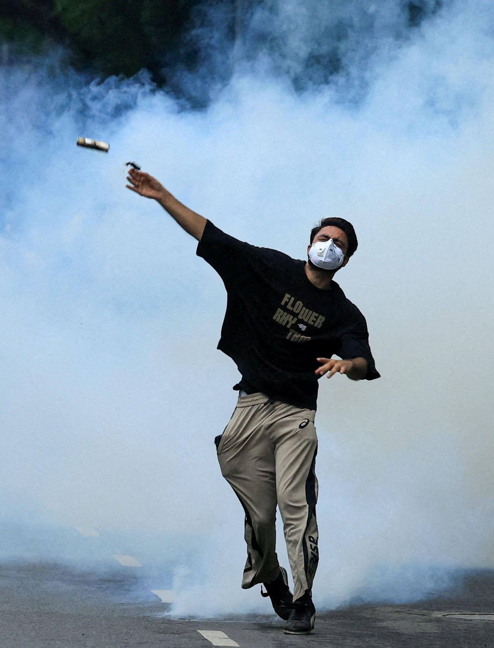 A protester throws back a tear gas canister toward police as supporters of the Cockroach Janta Party march on parliament in Delhi
