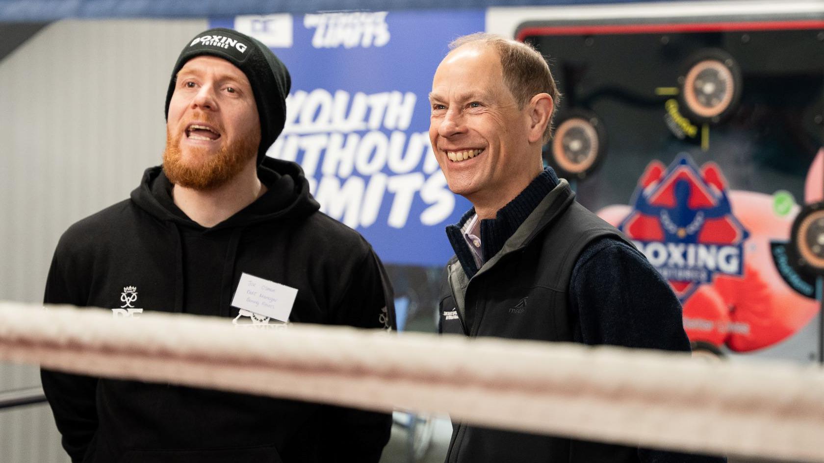 The Duke of Edinburgh stands outside of a boxing ring with Joe Osman who has a hat and beard.