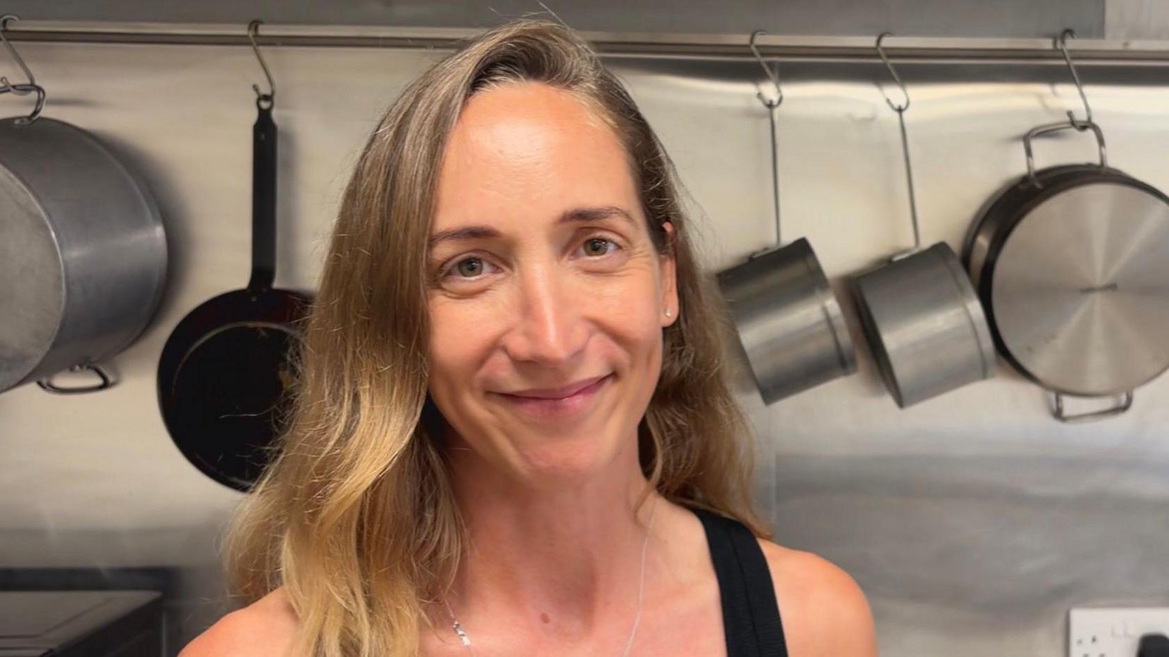Lady stood in a kitchen in front of pots and pans.