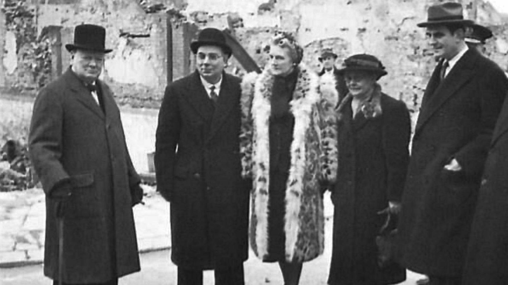 Black and white photograph of Winston Churchill, surveying the bomb damage in Swansea in 1941. Two women and two men, all wearing hats and coats, are with him