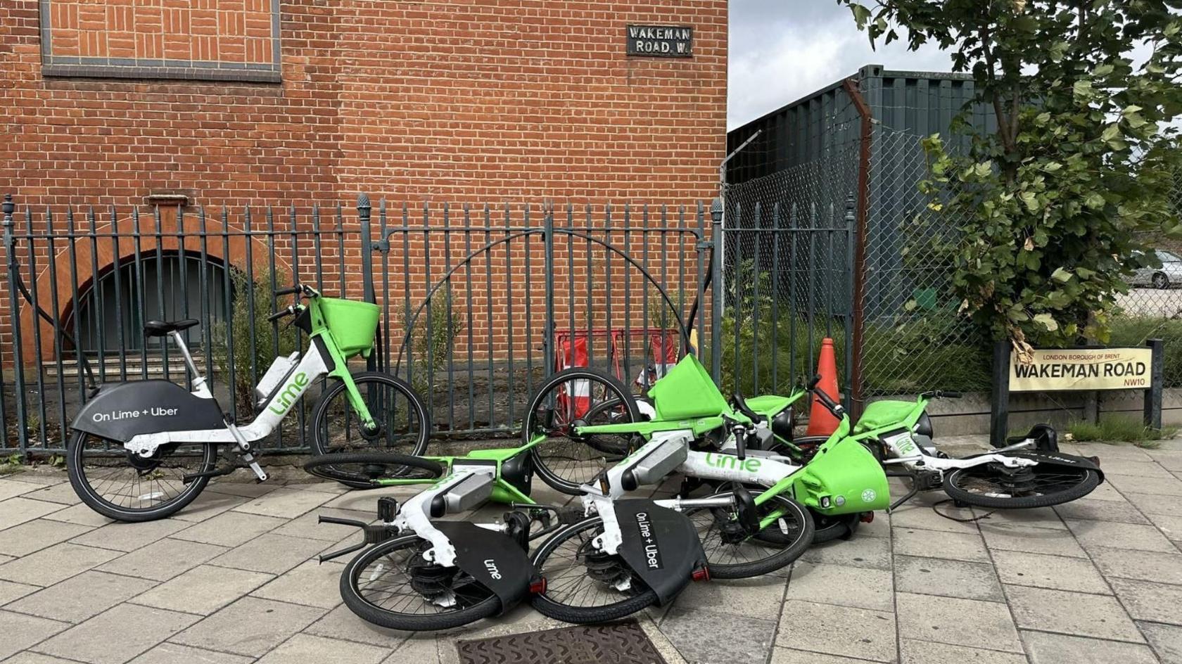 Six green Lime e-bikes, five of which have fallen on the floor on a pavement