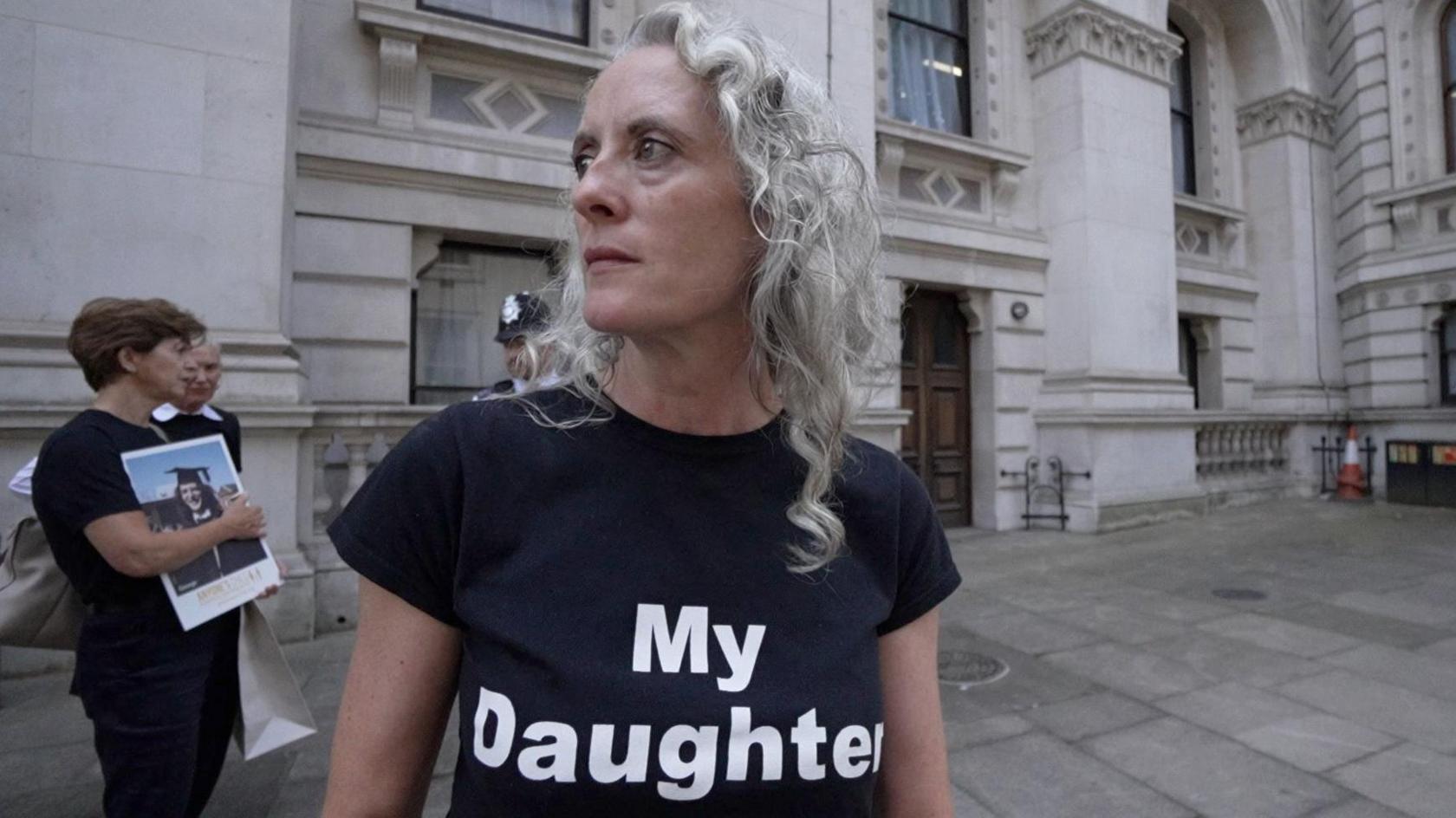 Anne-Marie Cockburn looking off to the side, wearing a black t-shirt that says "My Daughter".
