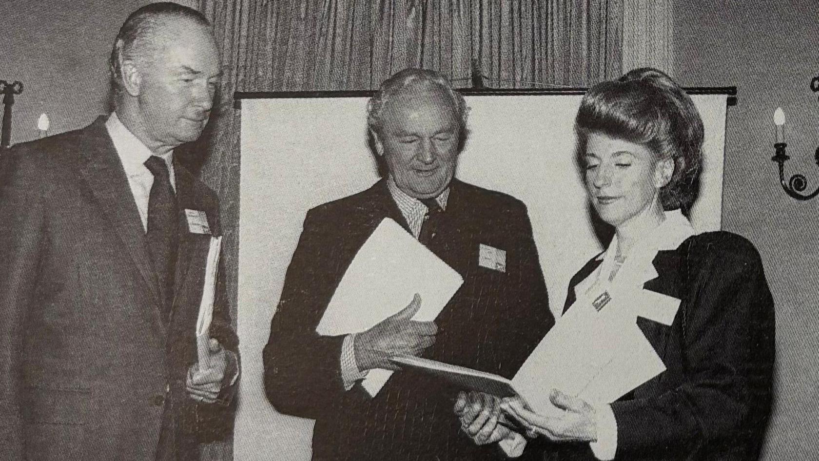 Two men and one woman staring into a brochure. The image was taken in 1993.