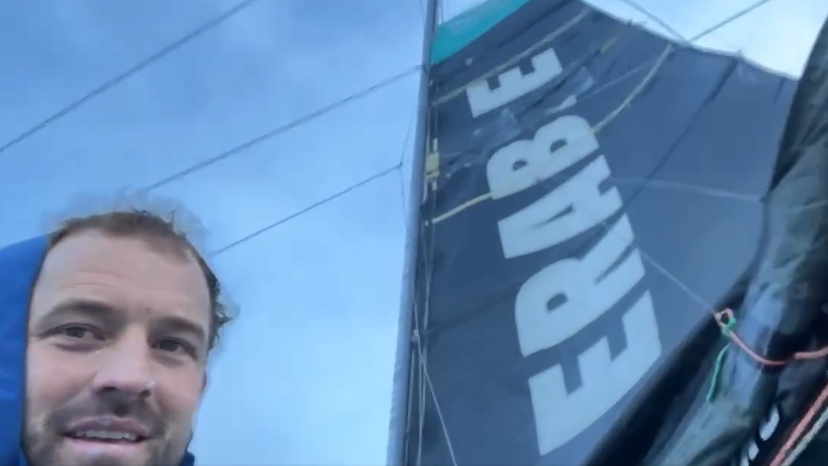 Sam Goodchild next to his repaired mainsail, which is black and has the word 'Vulnerable' written across it.