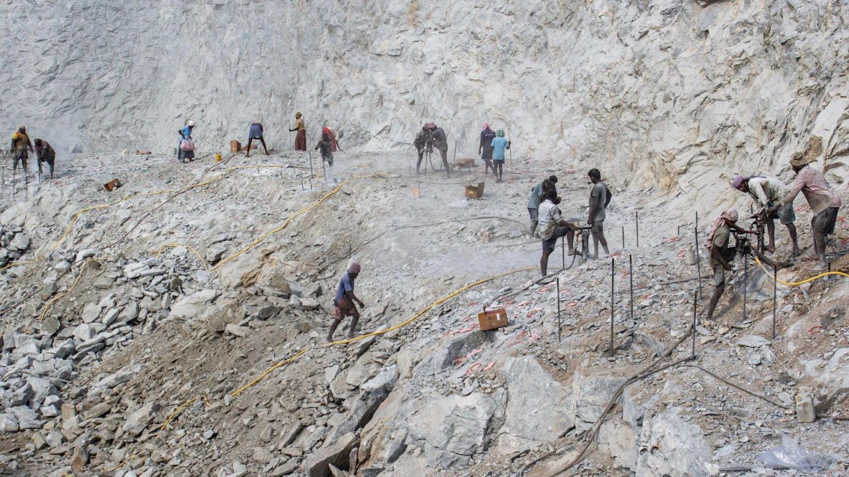 A landscape shot of a vast quarry showing numerous workers hard at work drilling, with yellow power cables snaking across the ground