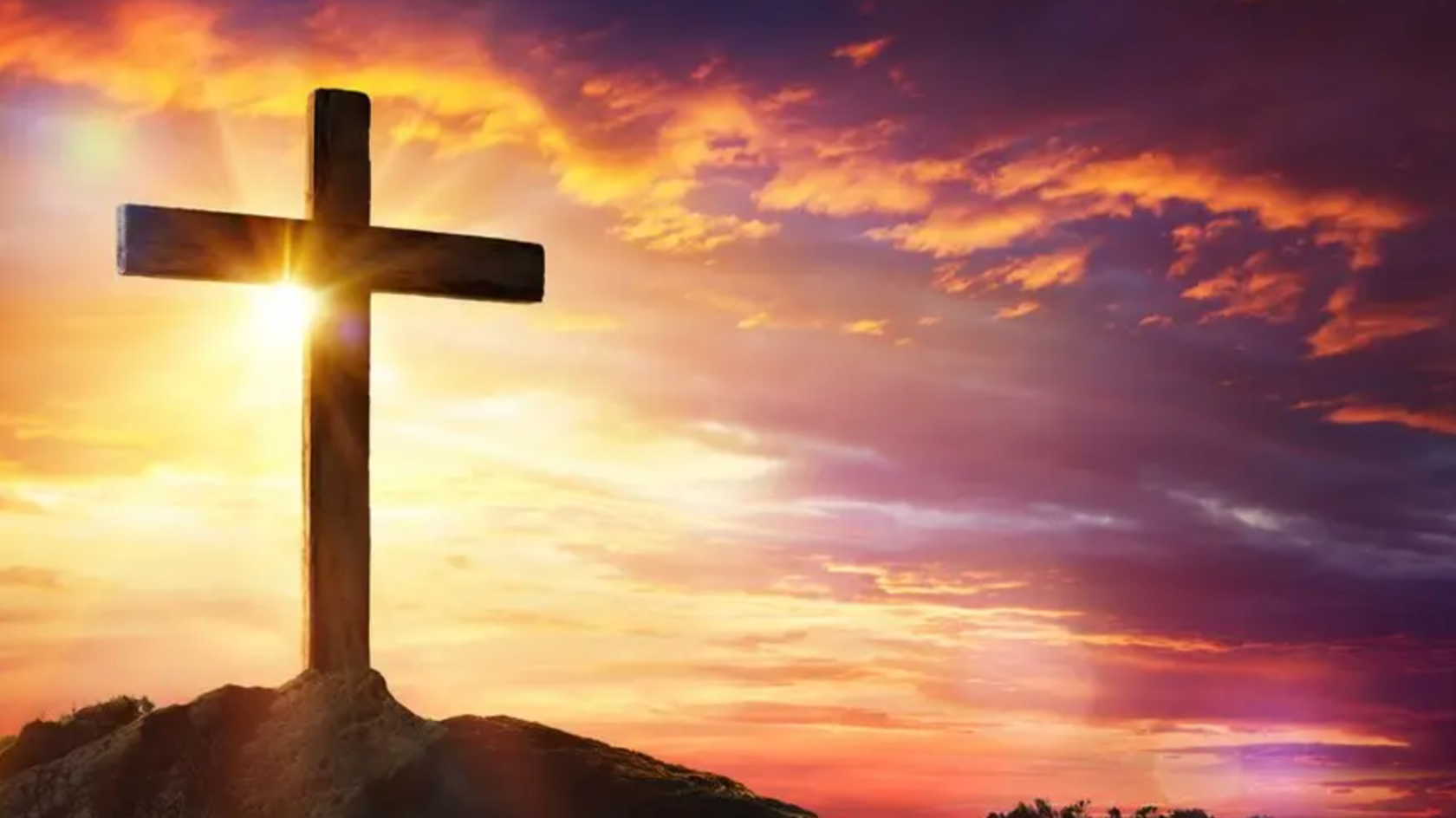 A wooden cross on a hill with a sunset behind.