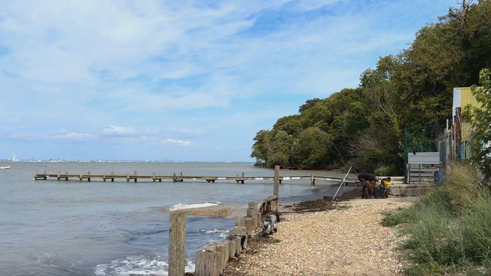 A sandy beach with wooden groynes. Beyond the sea is the Portsmouth coastline.
