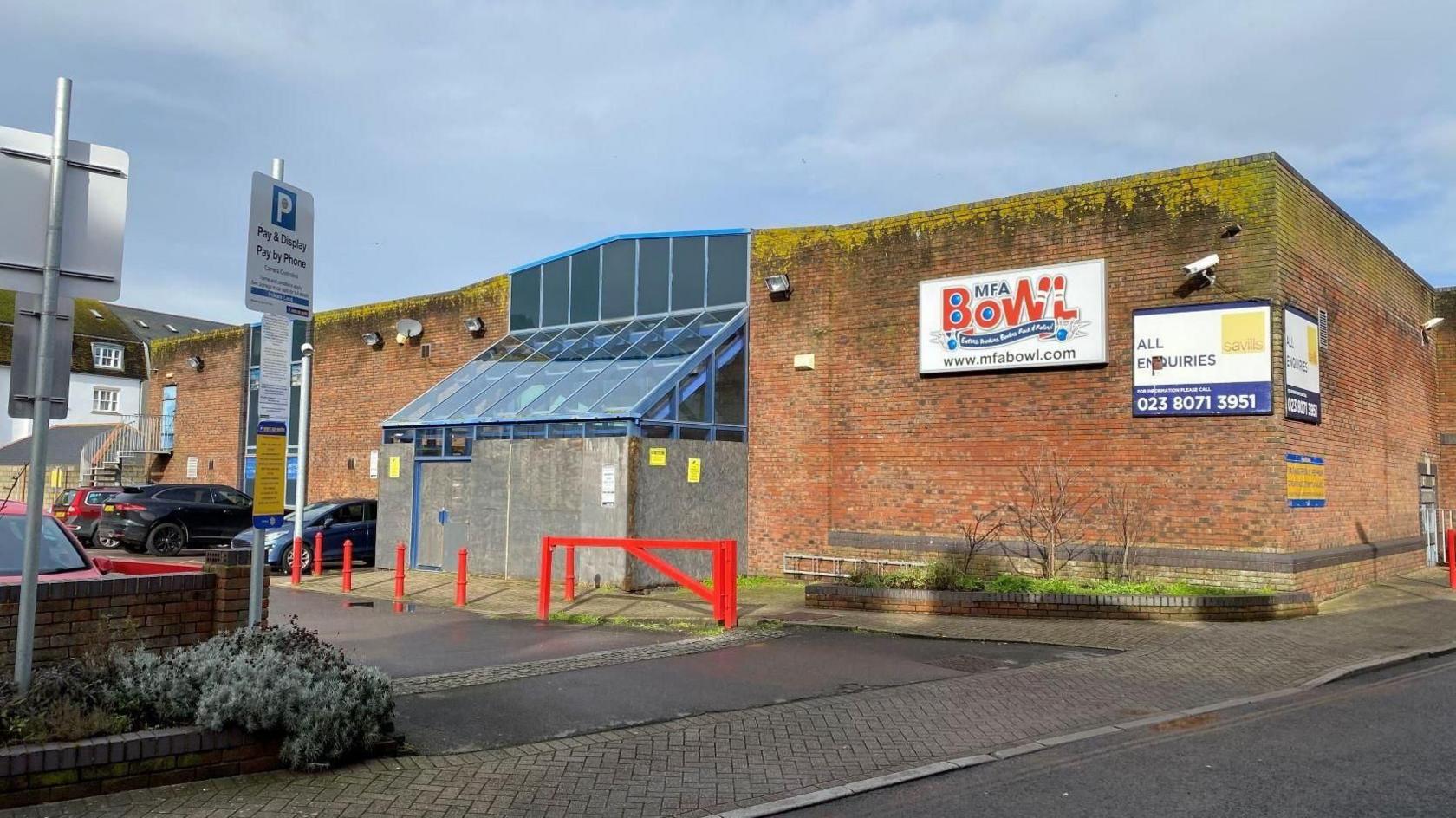 A general view of the outside of the bowling alley, which is evidently worn and has moss or some sort of growth at the top edge of the building