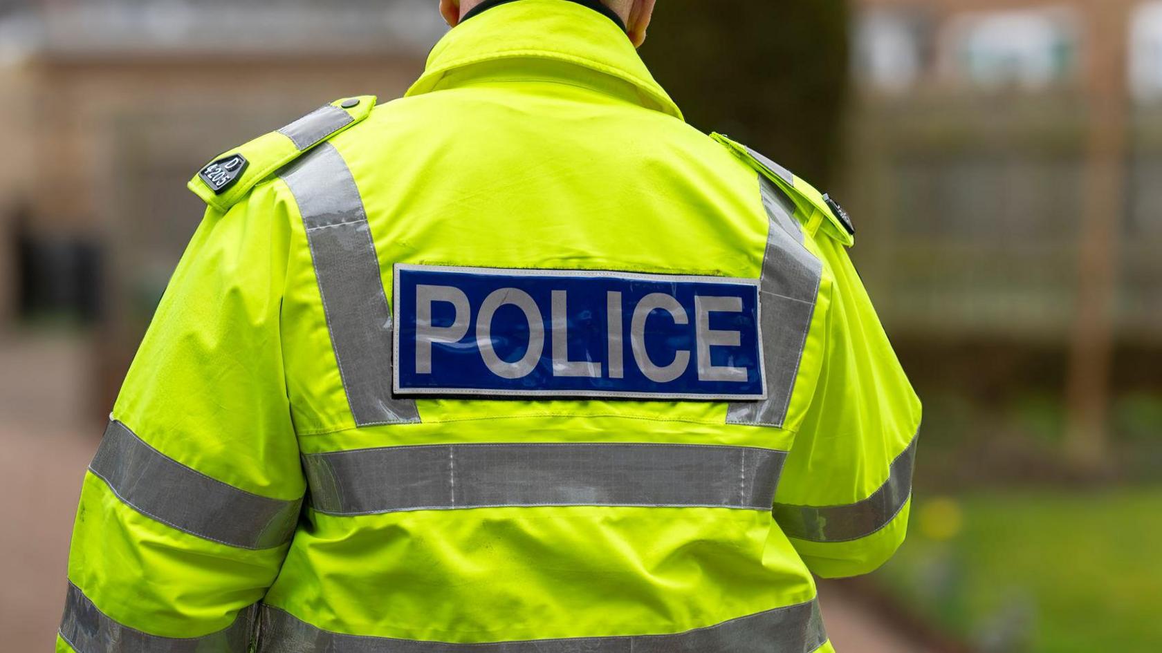 A policeman walking away from the camera on a residential street, which is out of focus.