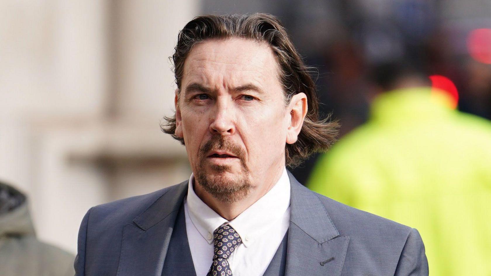 Richard hall, standing outside the High Court wearing a blue suit and speckled tie
