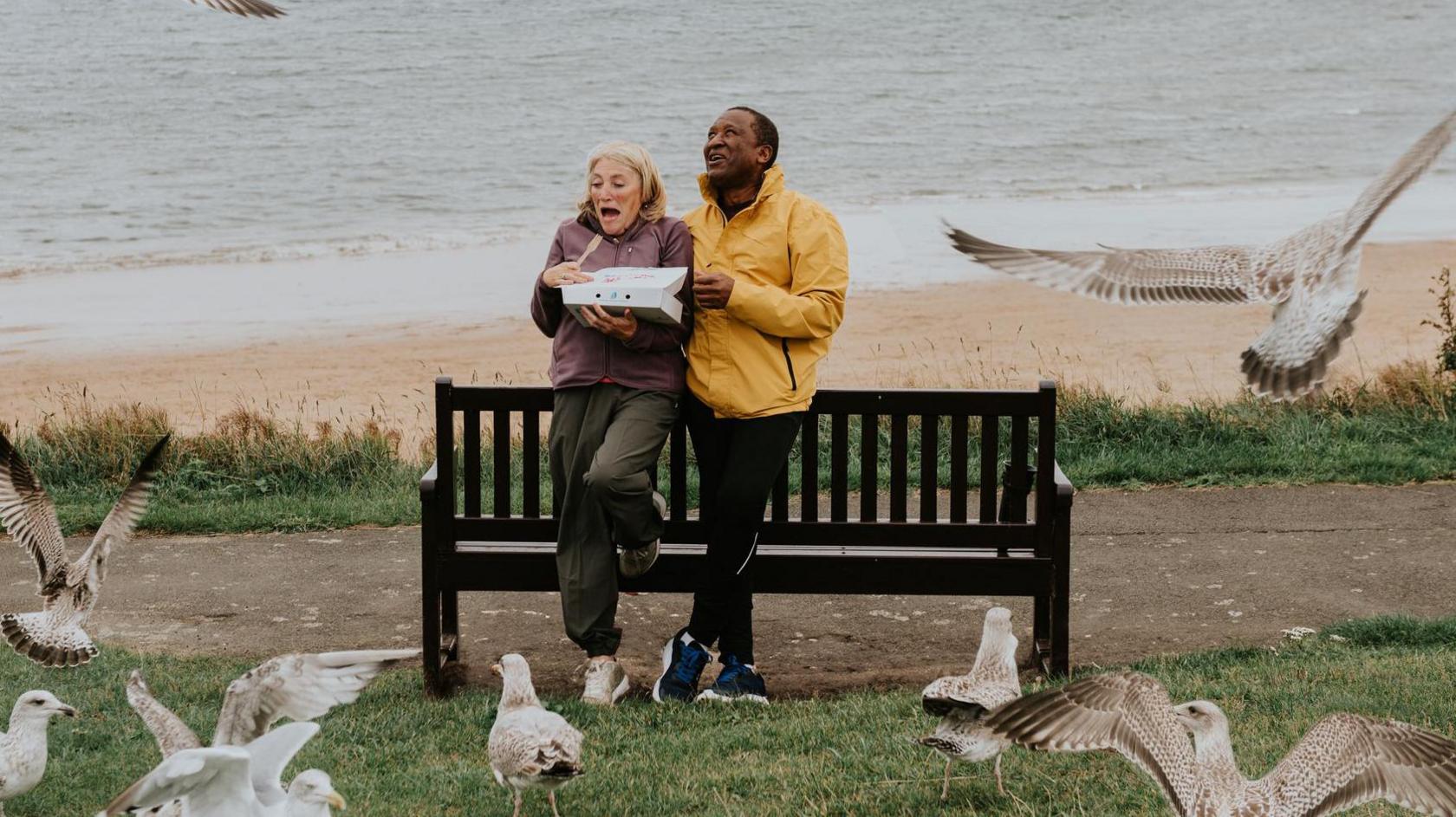 Opportunistic seagulls swoop down from the sky wanting to share in a couples portion of fish and chips.