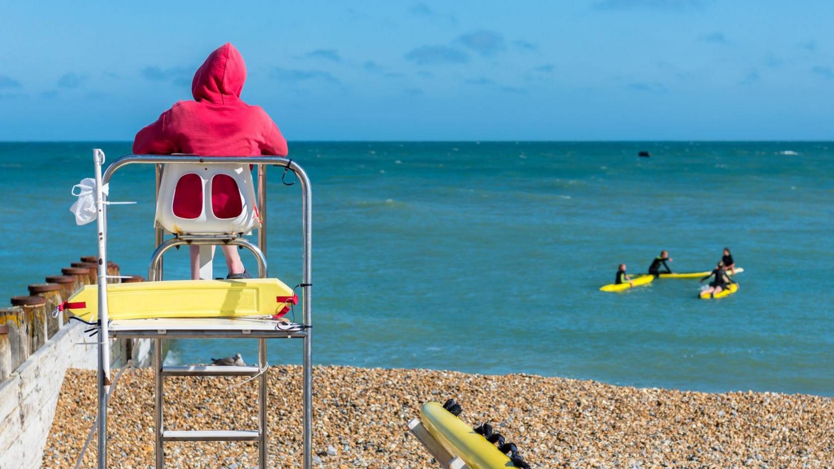 Rear view of a lifeguard sitting on a watchtower at the beach with surfers in the distance.