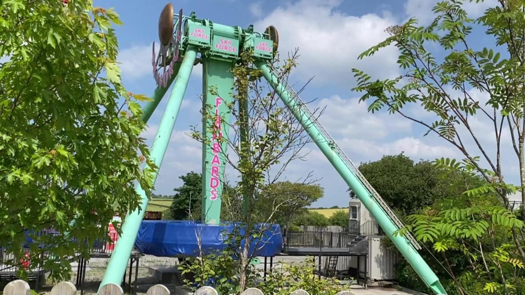 The turquoise-coloured Sky Force ride at Flambards theme park in Cornwall on a sunny day and surrounded by trees.