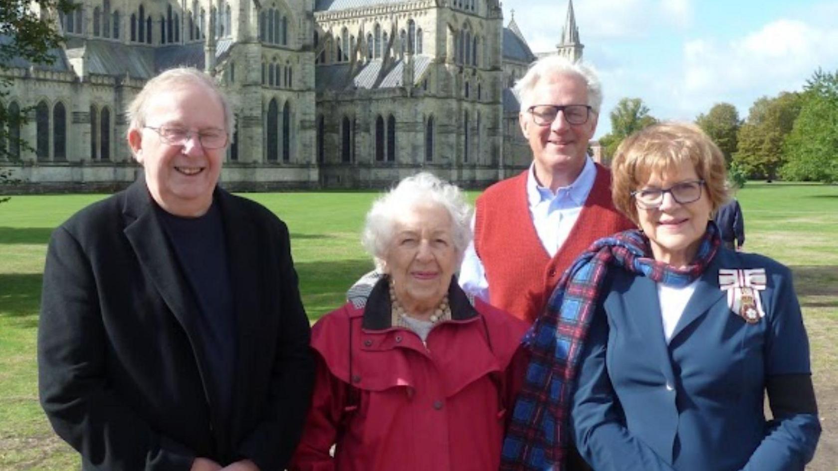 Dame Sarah Troughton, Lord Lieutenant of Wiltshire; Lord Margadale, Deputy Lieutenant; Phyll Babb; and Gordon Pardy of Salisbury Trust for the homeless stand in front of Salisbury cathedral on a sunny day
