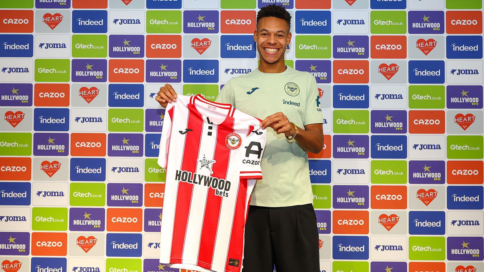 A smiling Kaye Furo holding up a Brentford shirt
