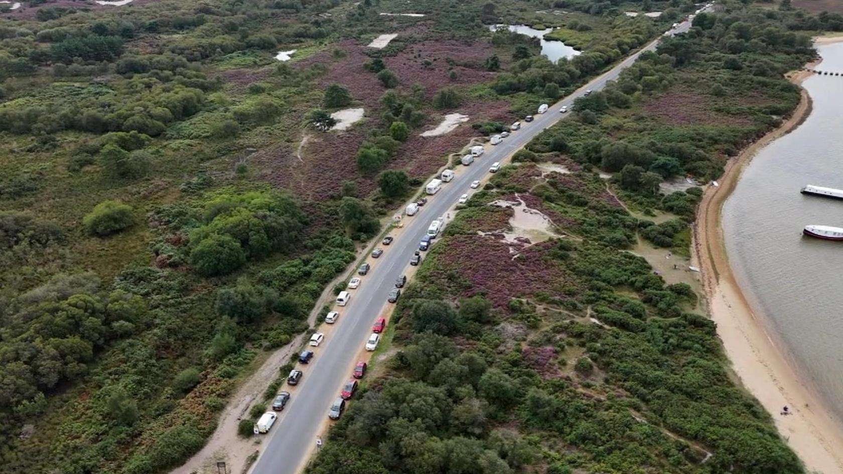 Drone view of the road through heathland with cars parked along both sides