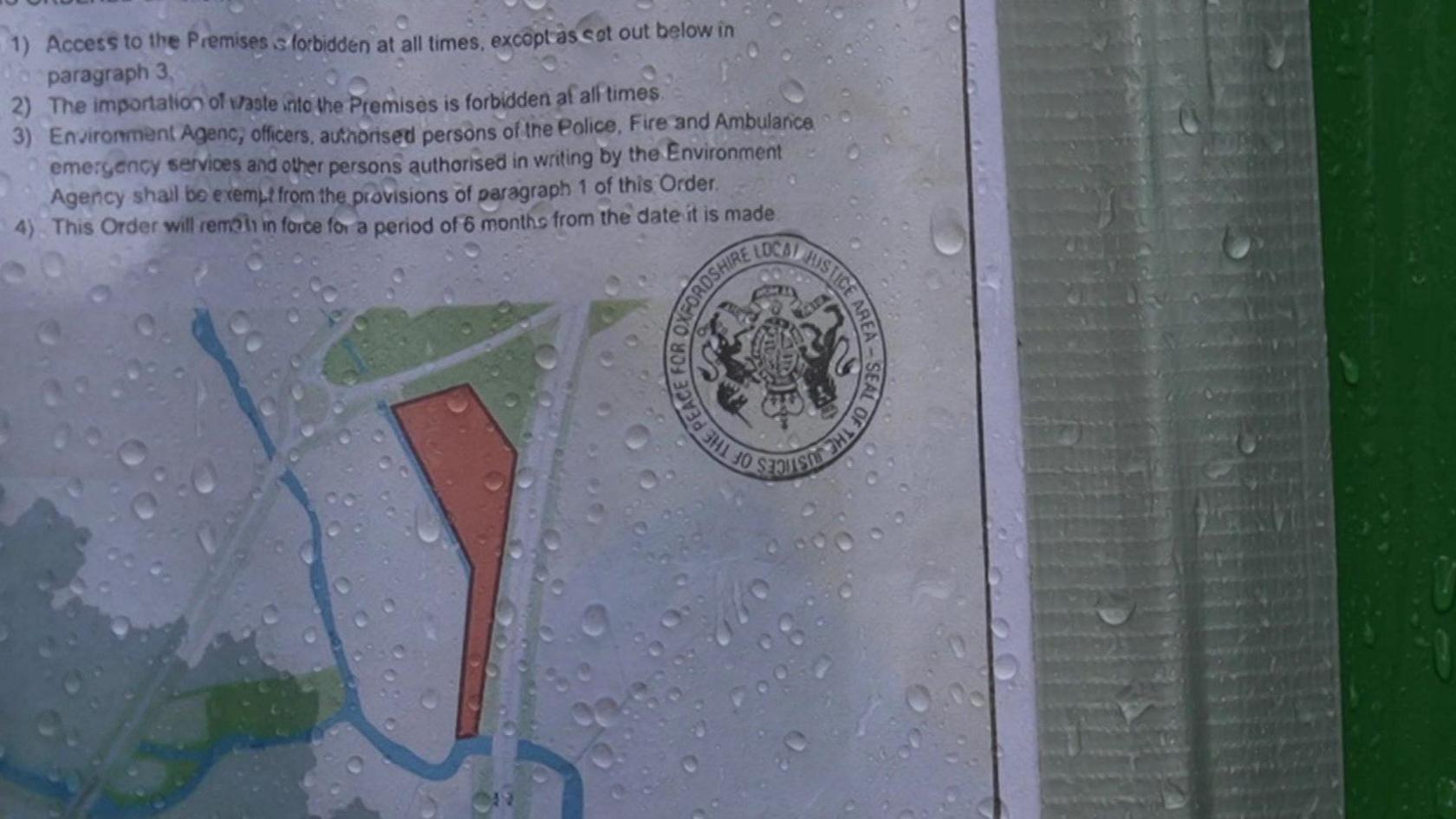 An order, fastened to a gate and covered in raindrops, shows the red area of the land that is now restricted.