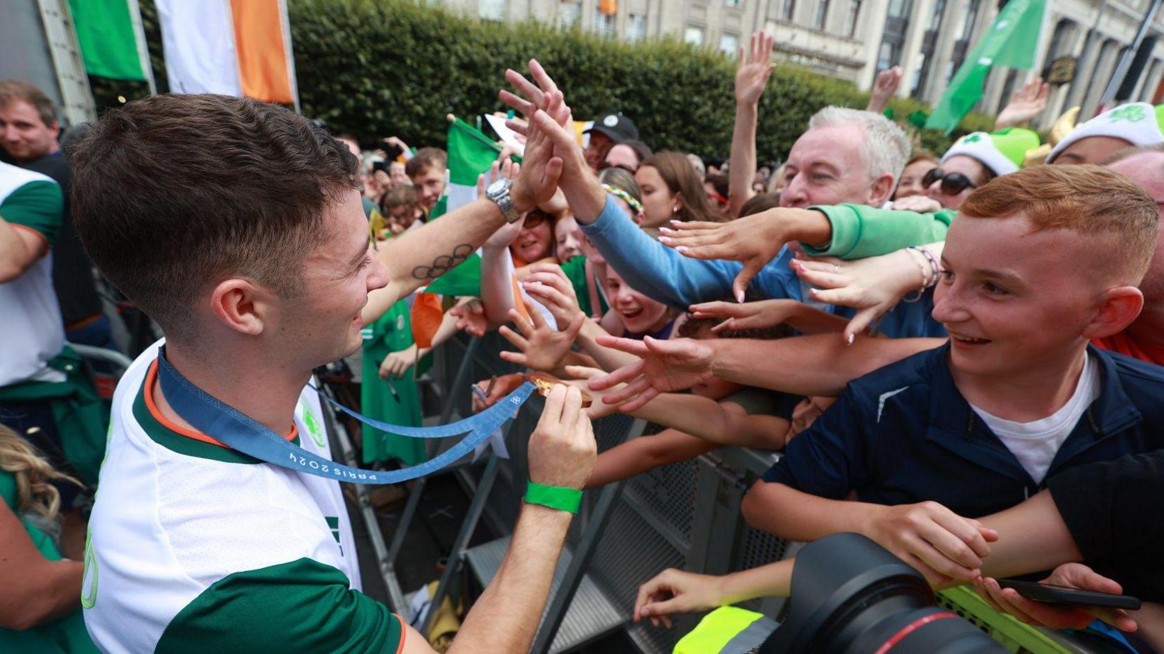 Rhys McClenaghan, wearing his gold medal and an Ireland top, is greeted by fans, including a young boy, in Dublin 