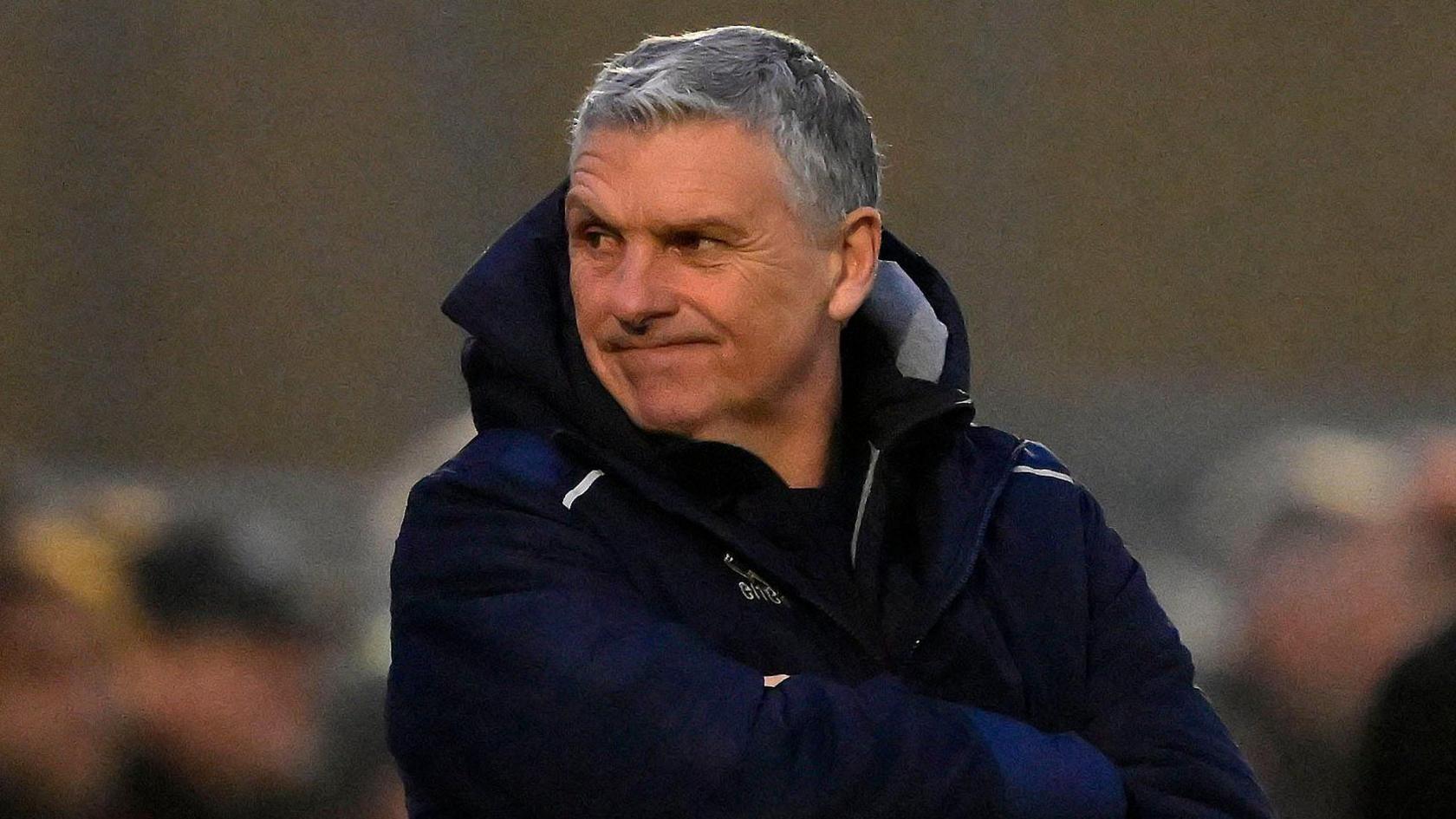 John Askey stood on the sidelines wearing a dark coat