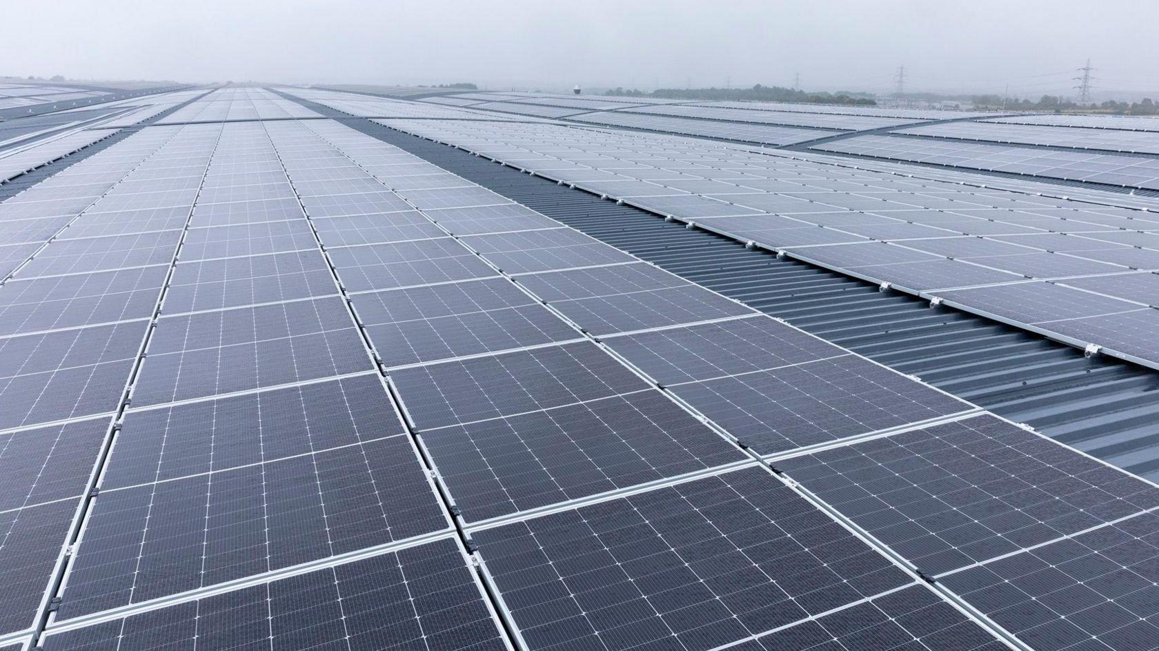 A roof with thousands of solar panels. There are some pylons in the distant background.