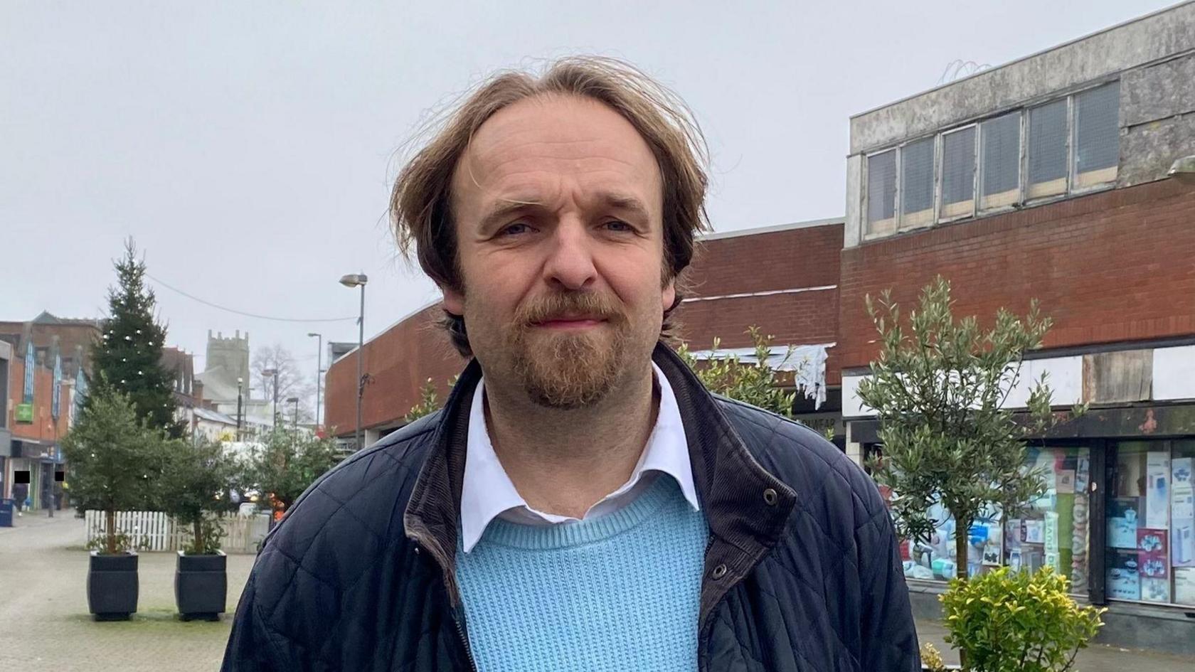 Robert Alden wearing a white shirt, a blue jumper and darker blue jacket stood in Erdington High Street