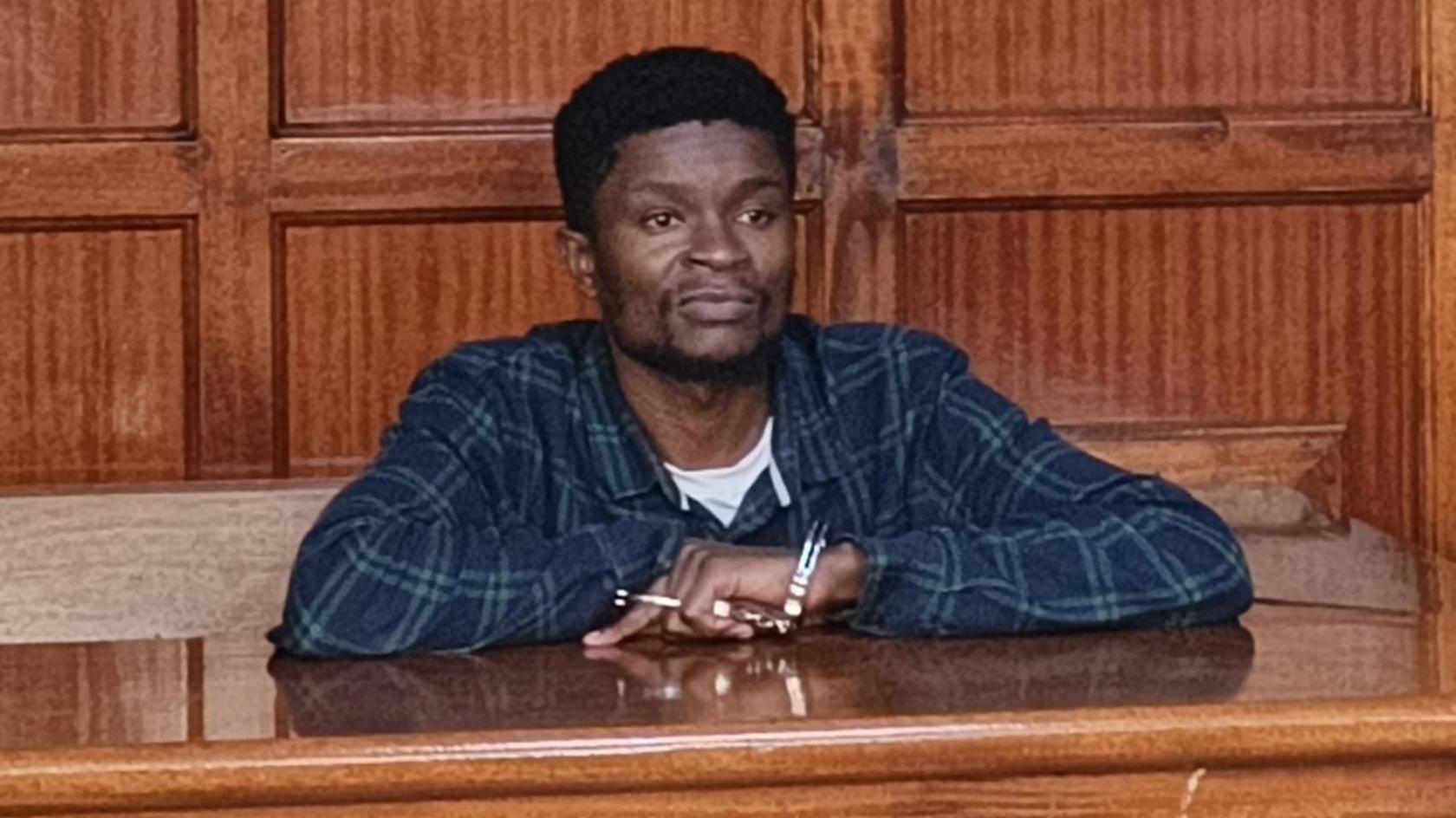 Webster Ochora Elijah in a checked shirt, behind the dock in court