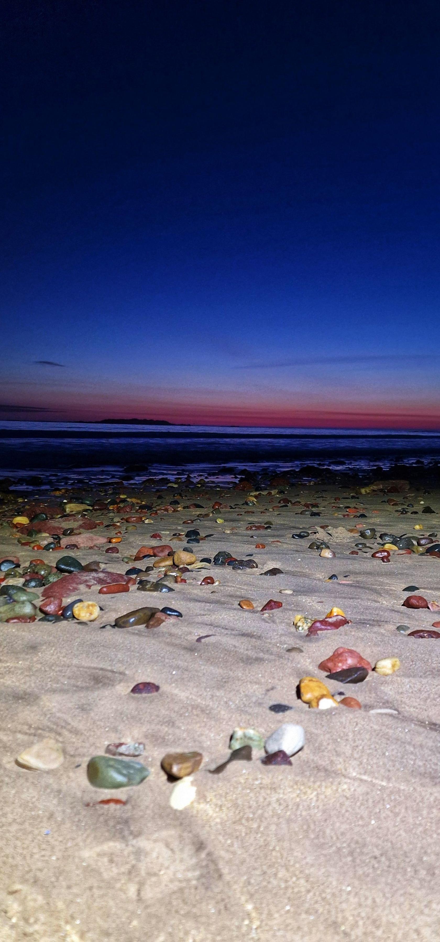 Colourful stones on the beach with a blue hued sunrise