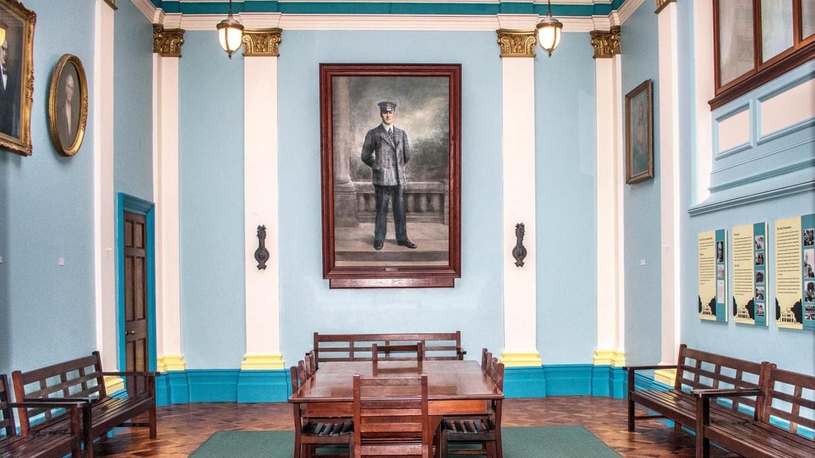 A large portrait of TB Davis on a blue and white wall. There is a table at the centre, with two benches either side. 