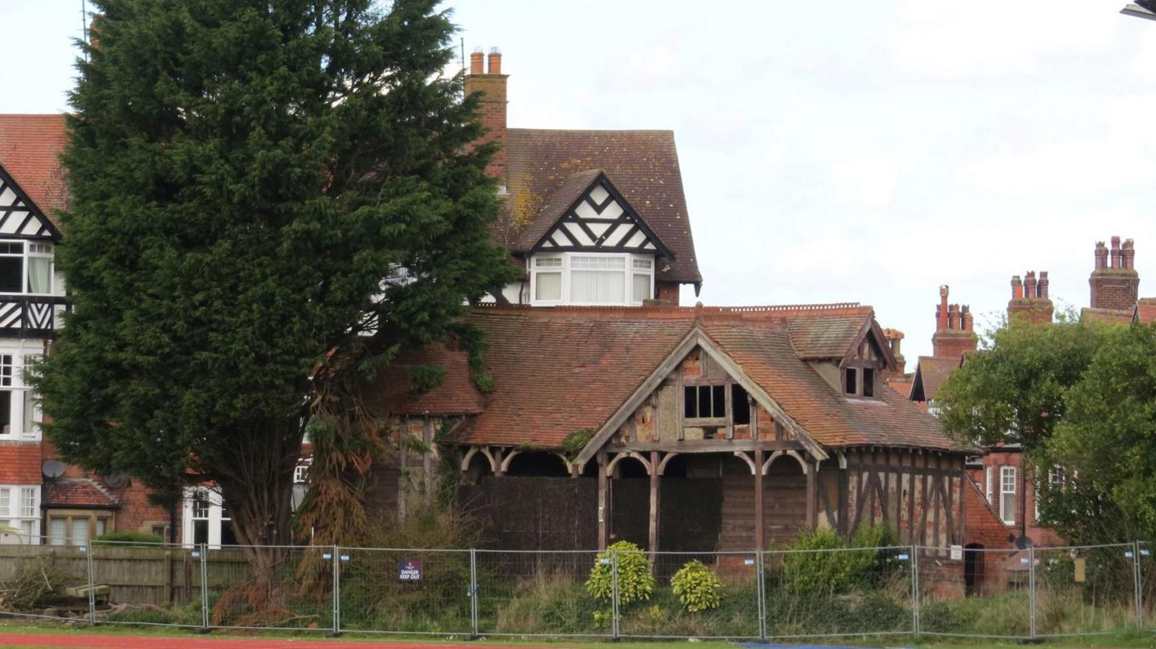 Safety fencing surrounds the derelict tennis pavilion