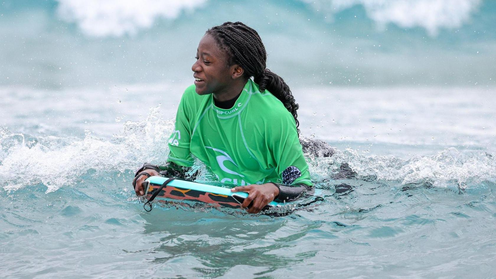 A teenage girl in a green top bodyboards on a wave at The Wave surfing lake in Bristol