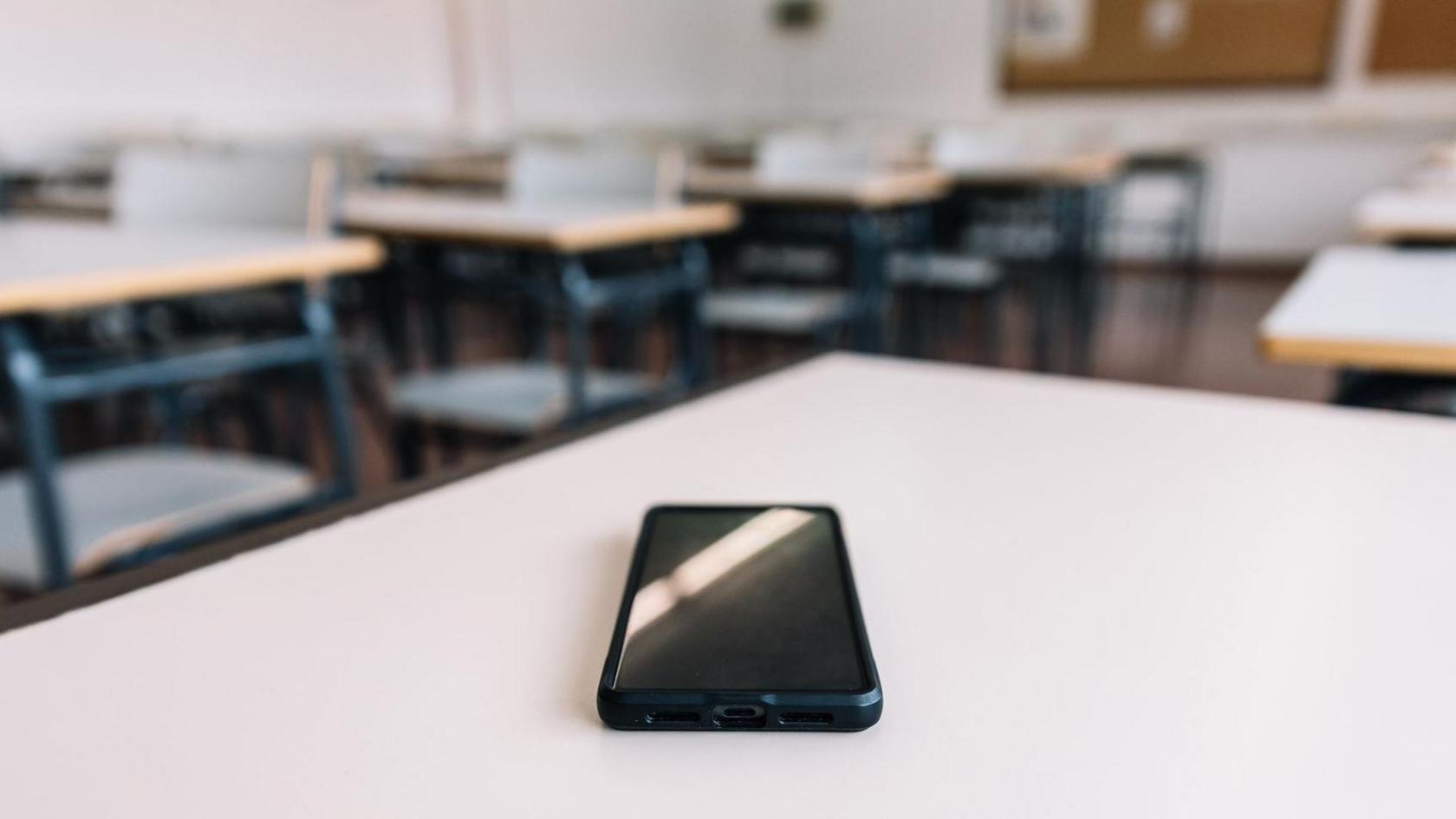 A phone lies face up on a classroom table