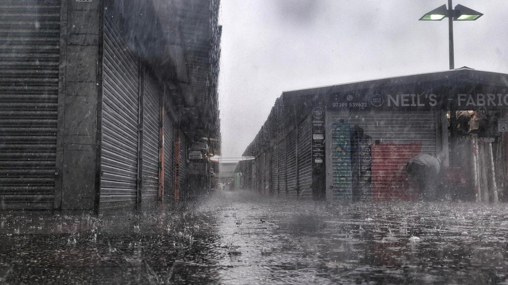 Heavy rain pours in a deserted street in front of an urban scene with shops and warehouses