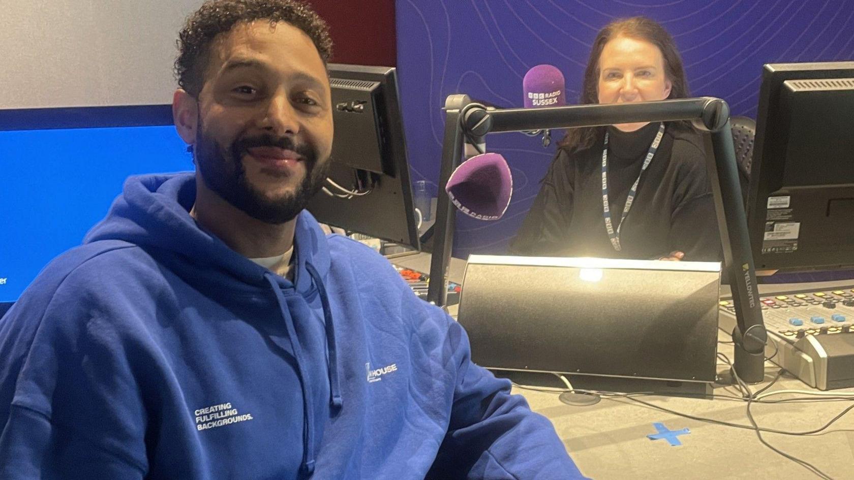 A man in a blue hoodie in a recording studio. 