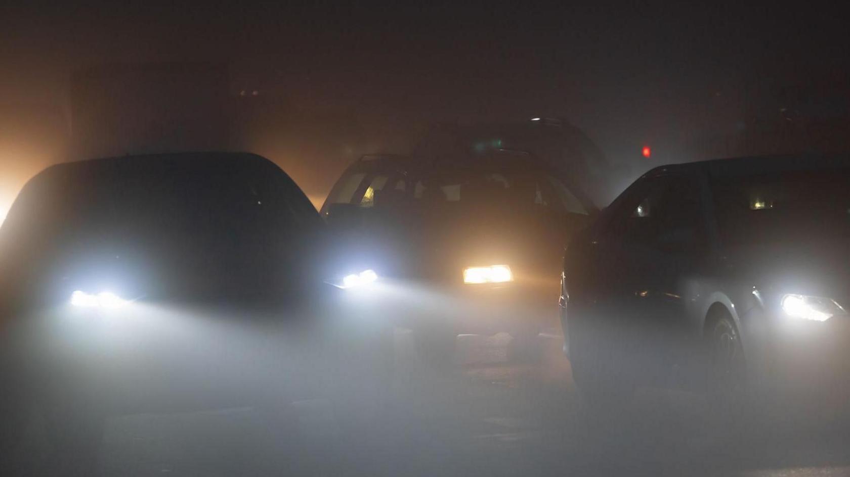 Three sets of car headlights shining in the dark