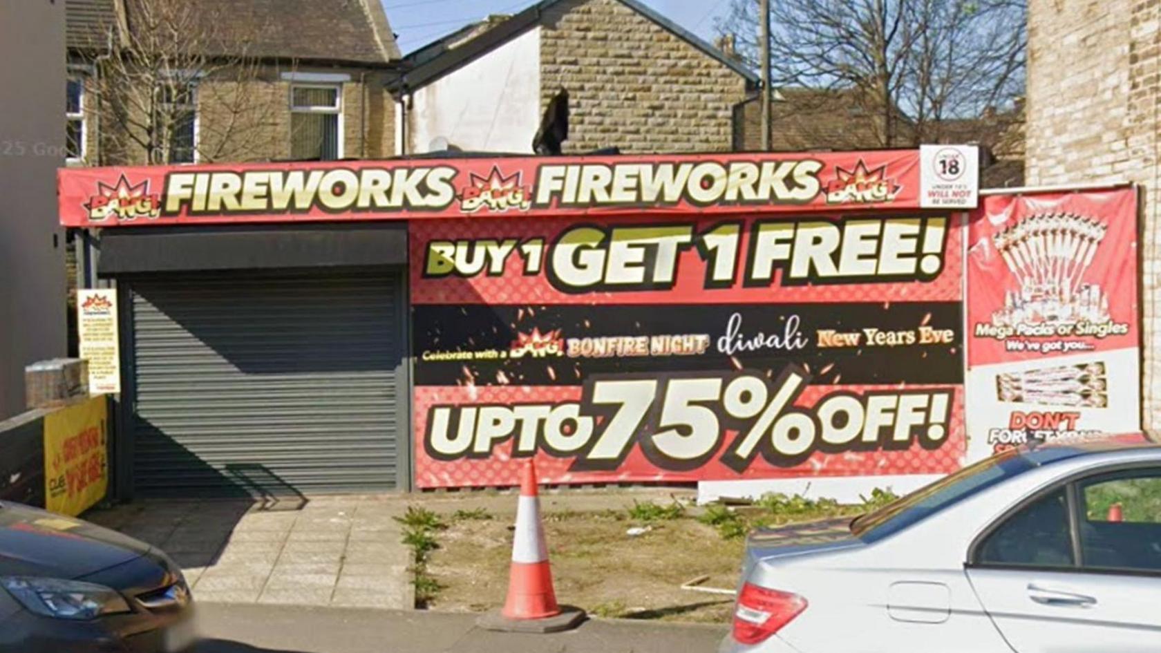 A fireworks shop, as indicated by its signage. Its signage is brash, features red and yellow colours and includes writing such as 'Buy 1 Get 1 Free!' and 'Up to 75% off'