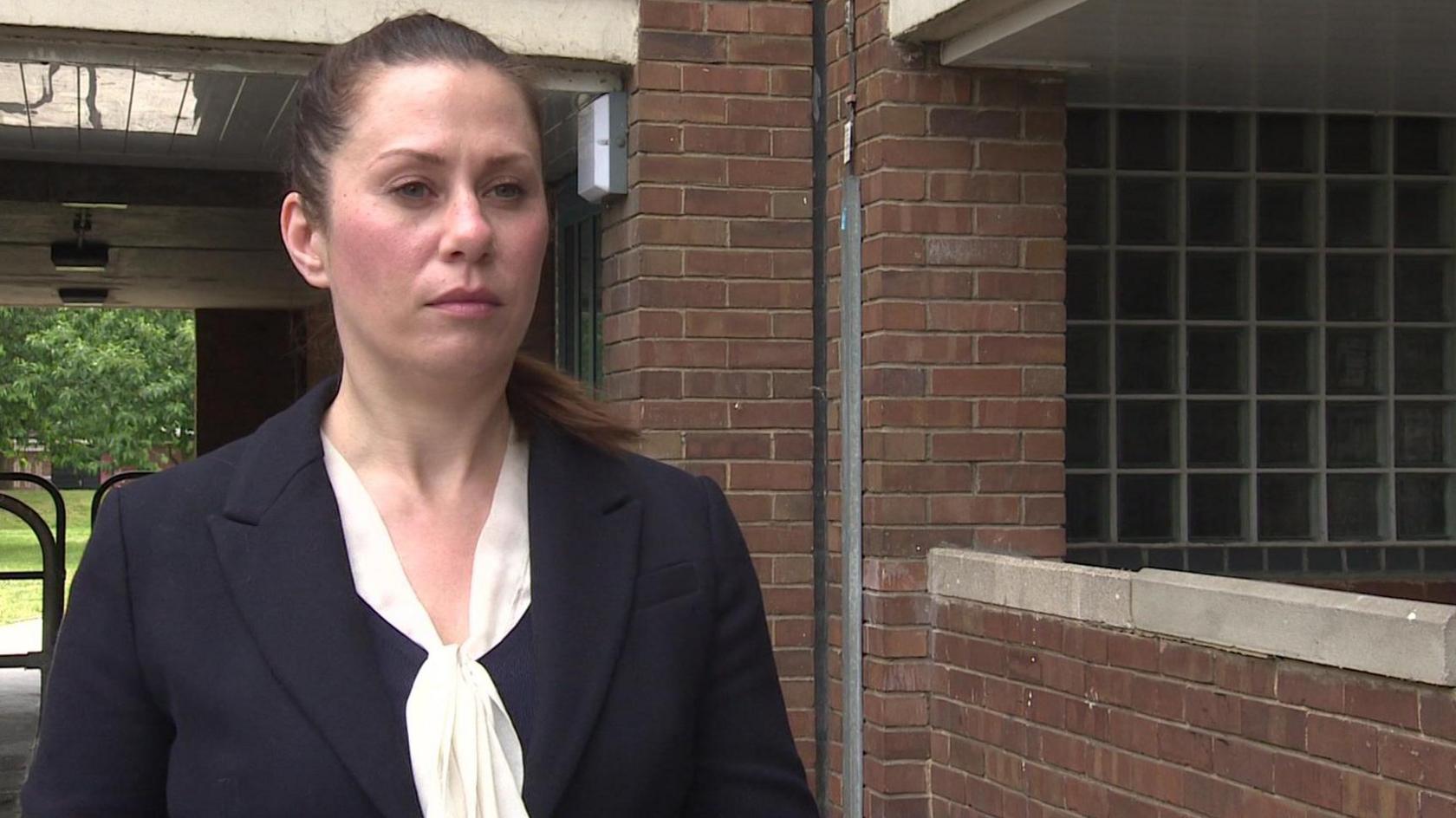 Det Ch Insp Becky Woodsford, a woman wearing a smart navy jacket with a white blouse and has dark hair in a ponytail. She is standing in a housing estate